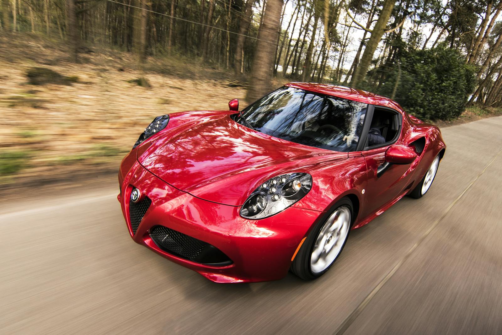 A sleek red sports auto driving fast on a forest road, showcasing speed and luxury.